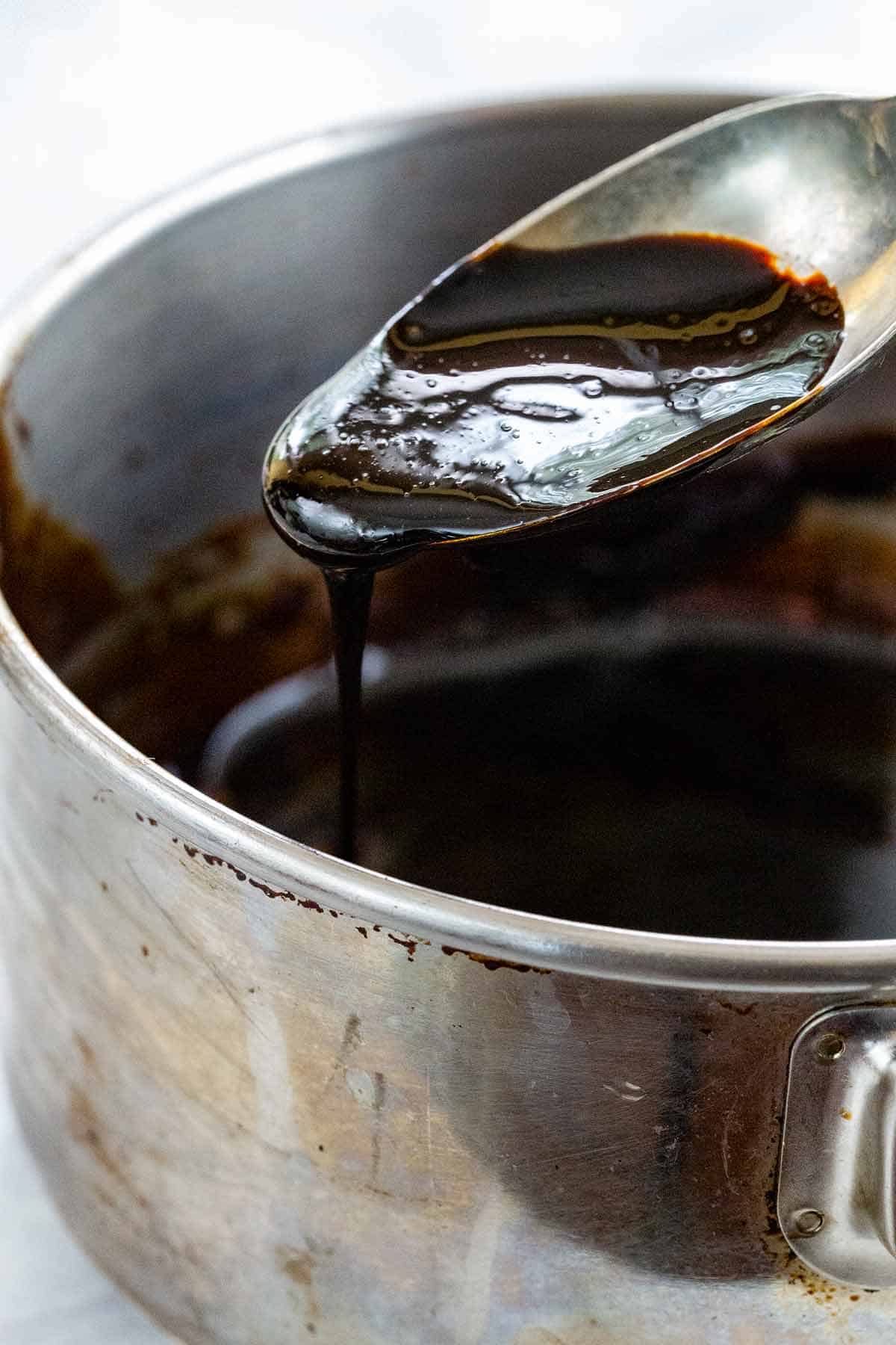 Thick, dark balsamic reduction dripping from a metal spoon into a saucepan