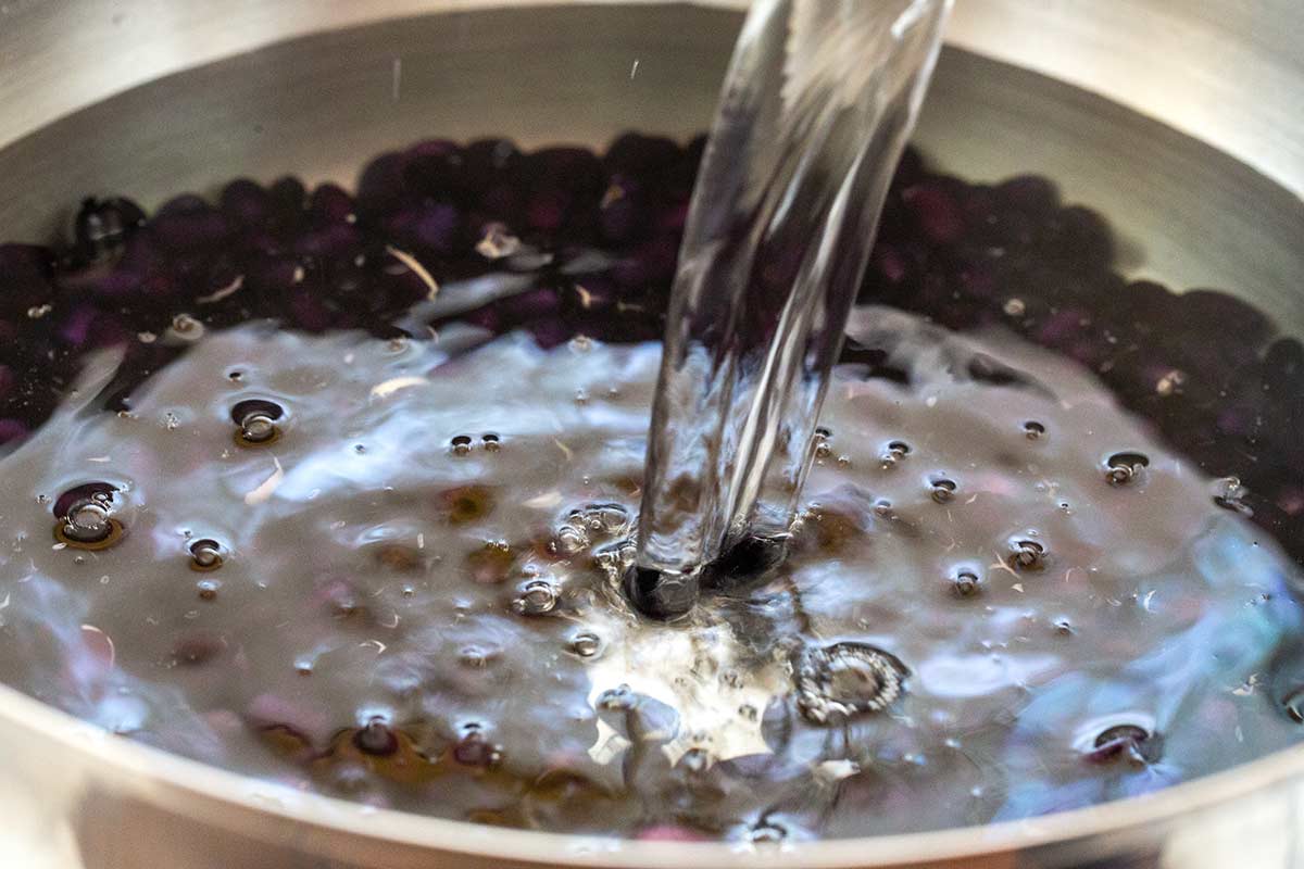 Water pouring over dried black beans in a stainless steel bowl to rinse them.