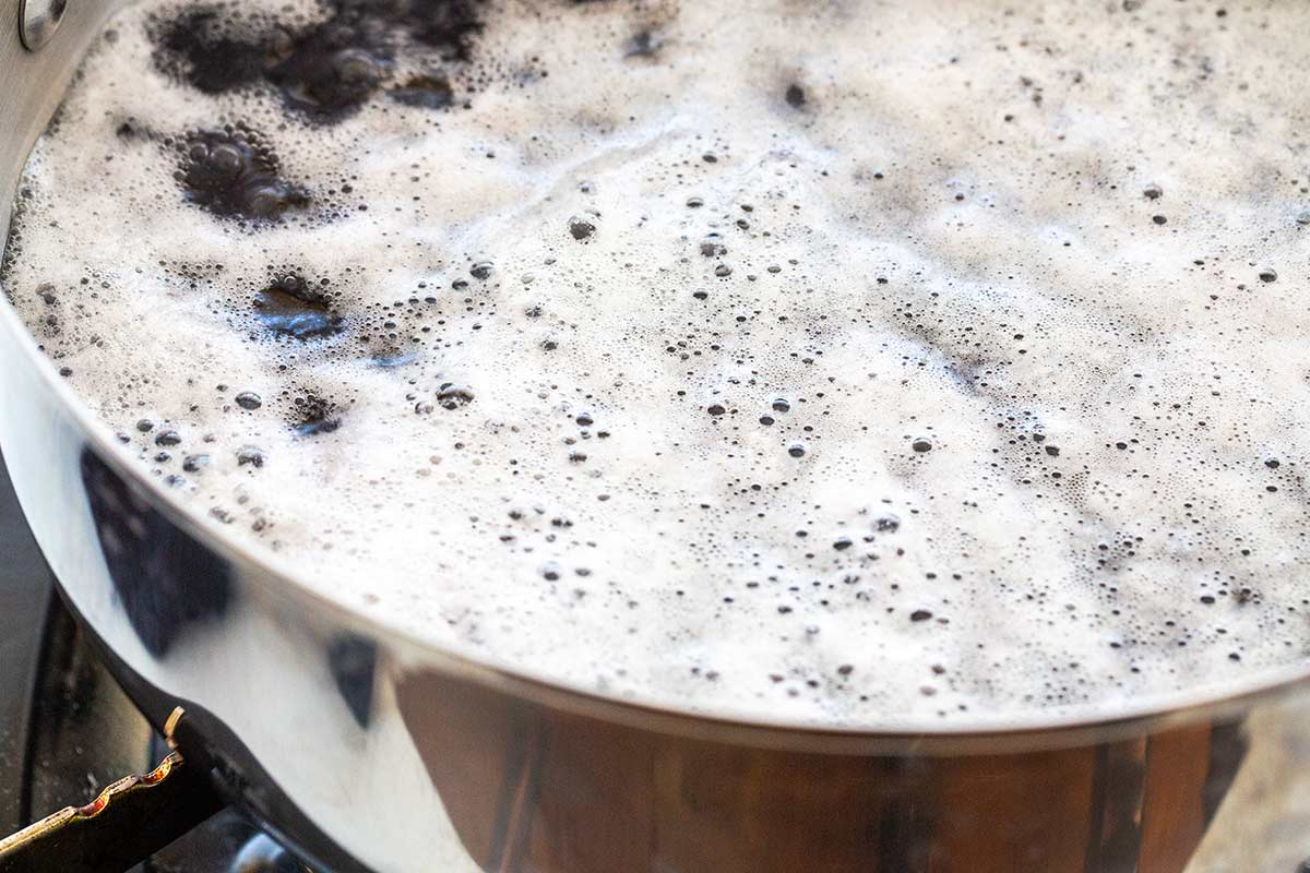Black beans simmering in a pot on the stovetop with foam on top of the water.