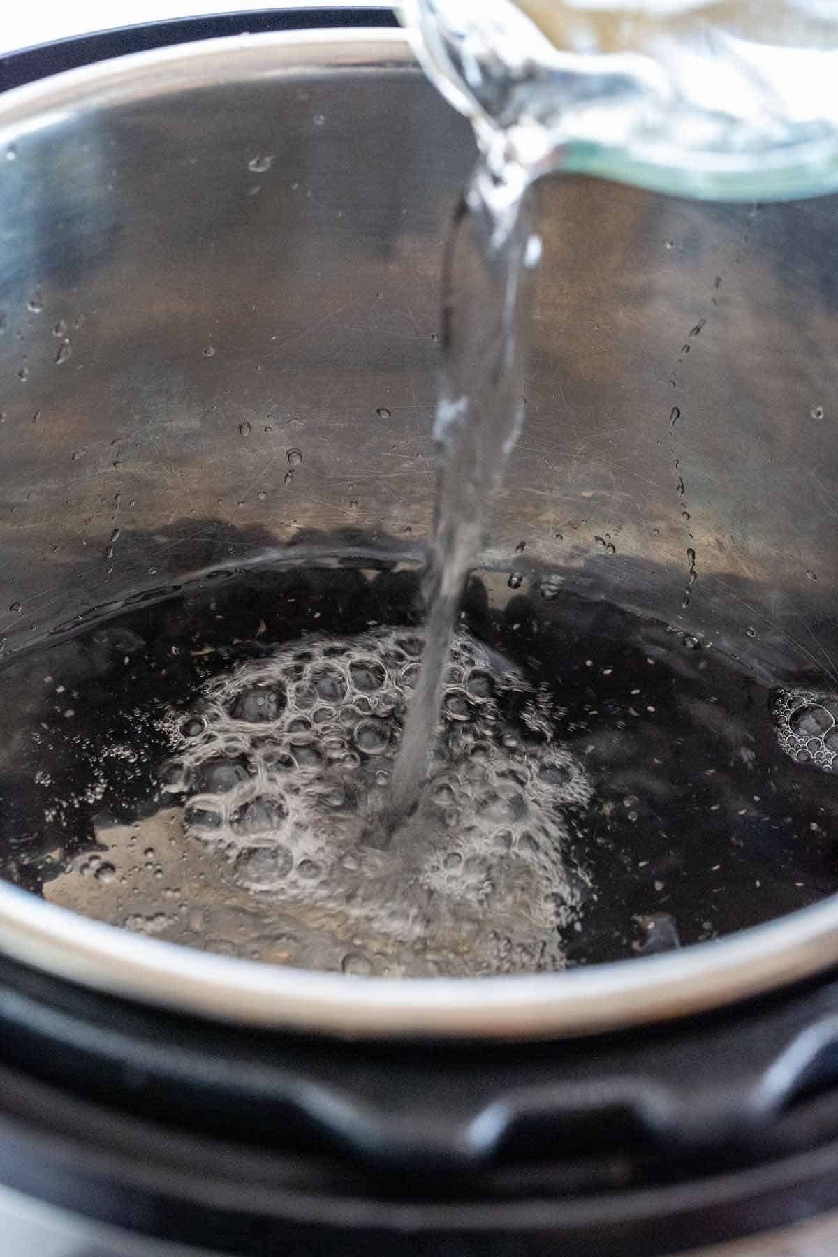 Pouring water into an Instant Pot insert filled with dry black beans.