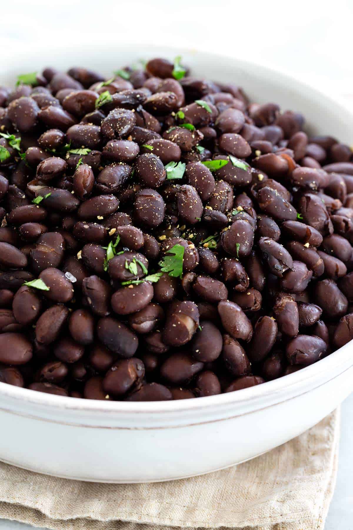 Cooked black beans garnished with fresh cilantro and seasoning in a white bowl.
