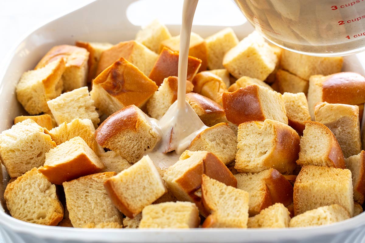 Liquid custard being poured into a baking dish with toasted cubes of bread.