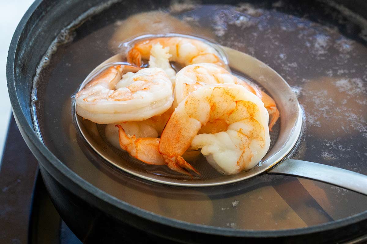 Metal strainer lifting cooked shrimp out of a pot of water.