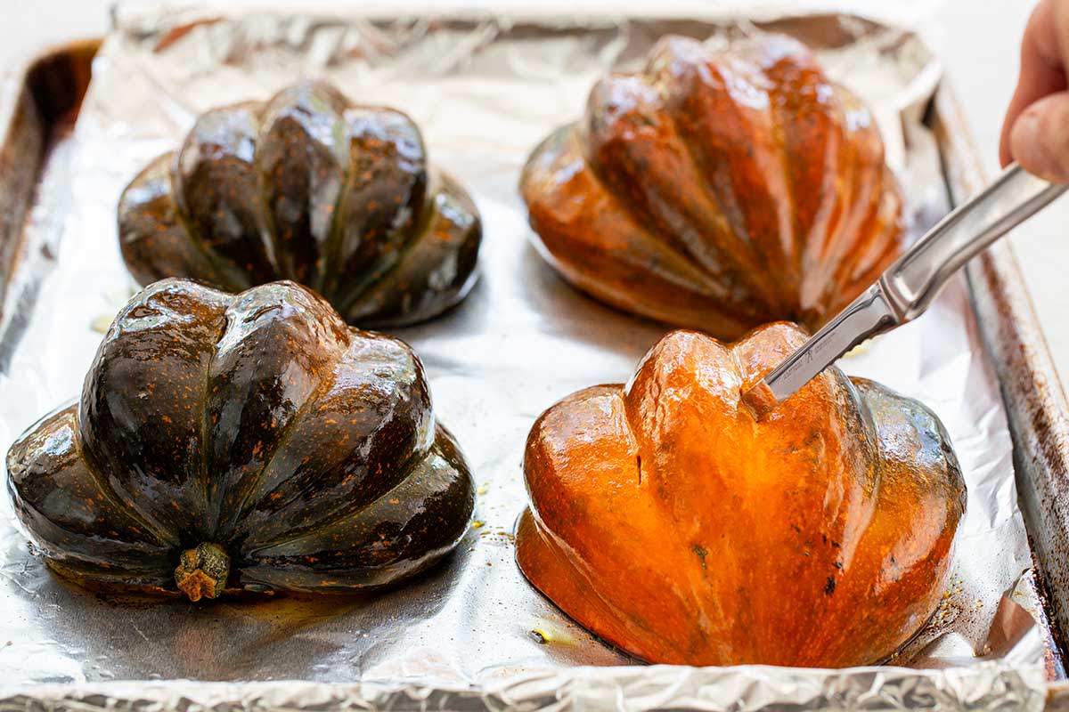 Brushing olive oil onto acorn squash halves placed cut-side down on a foil-lined baking sheet.