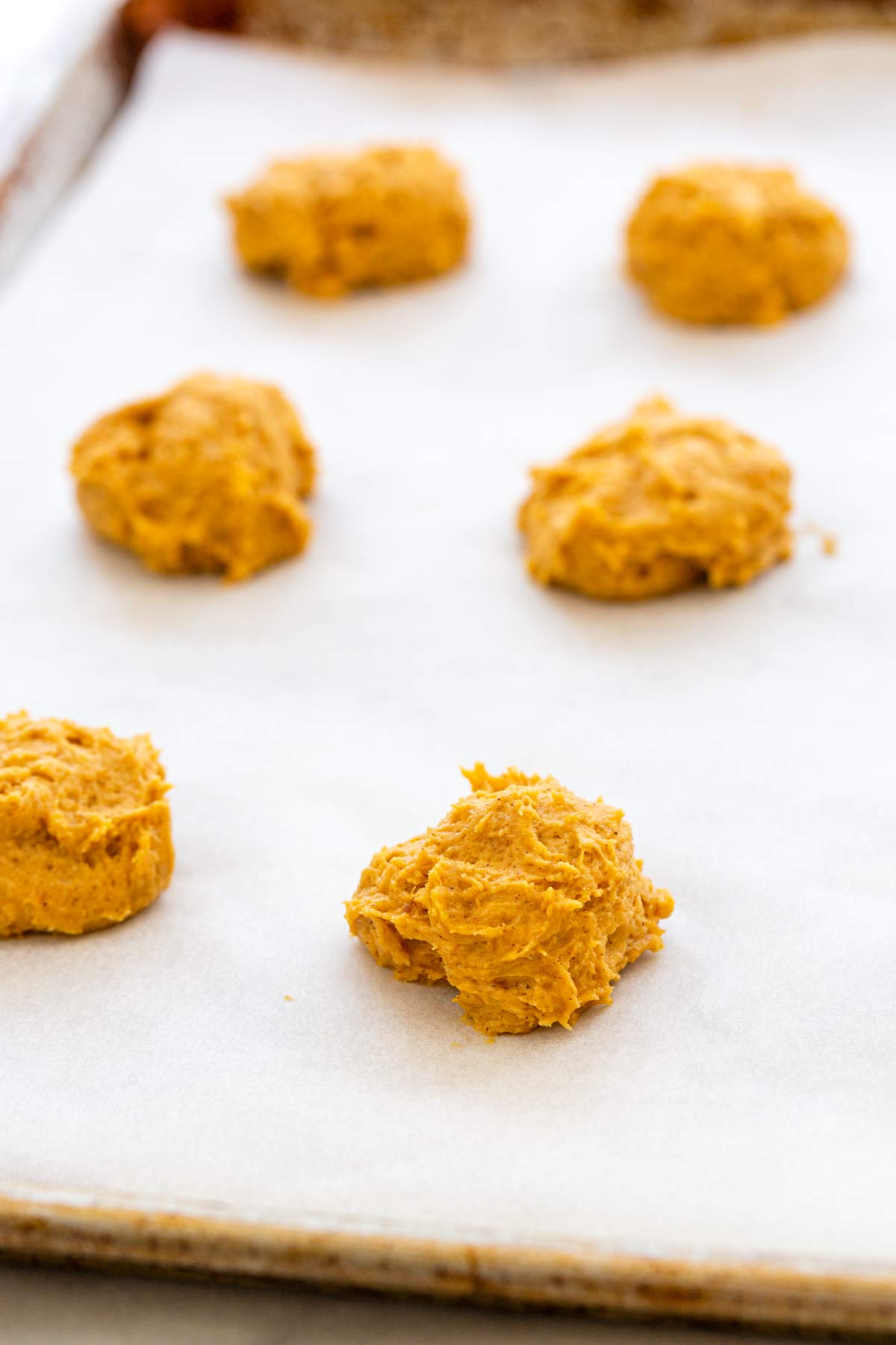 Several scoops of pumpkin cookie dough placed on a paper lined sheet pan.