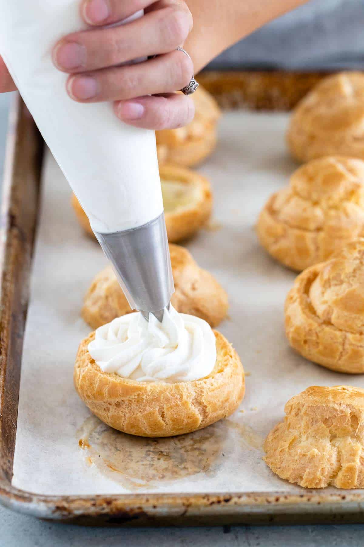 Jessica pipping the whipped cream filling into a cream puff bottom.