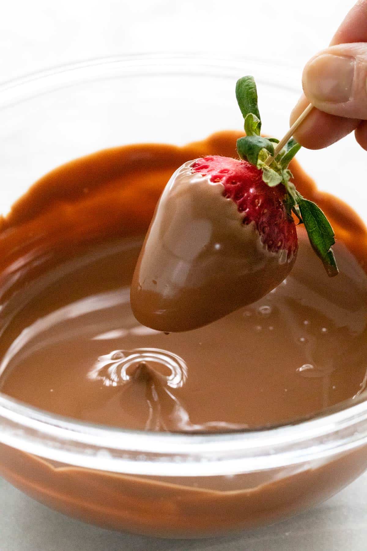 Dipping a strawberry into a bowl of melted chocolate.