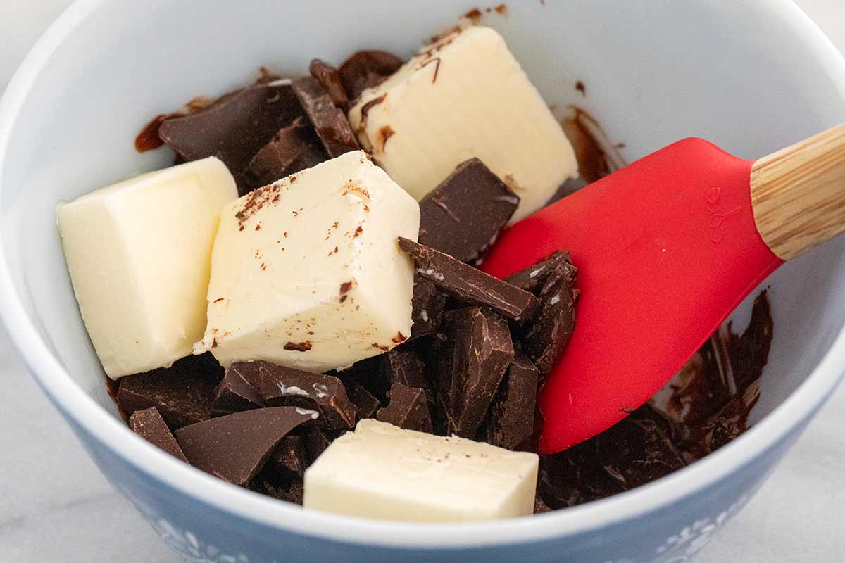 Slices of butter and broken pieces of chocolate bar in a bowl with a spatula.