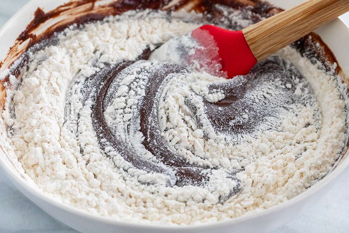 Flour being mixed into a bowl of chocolate batter.