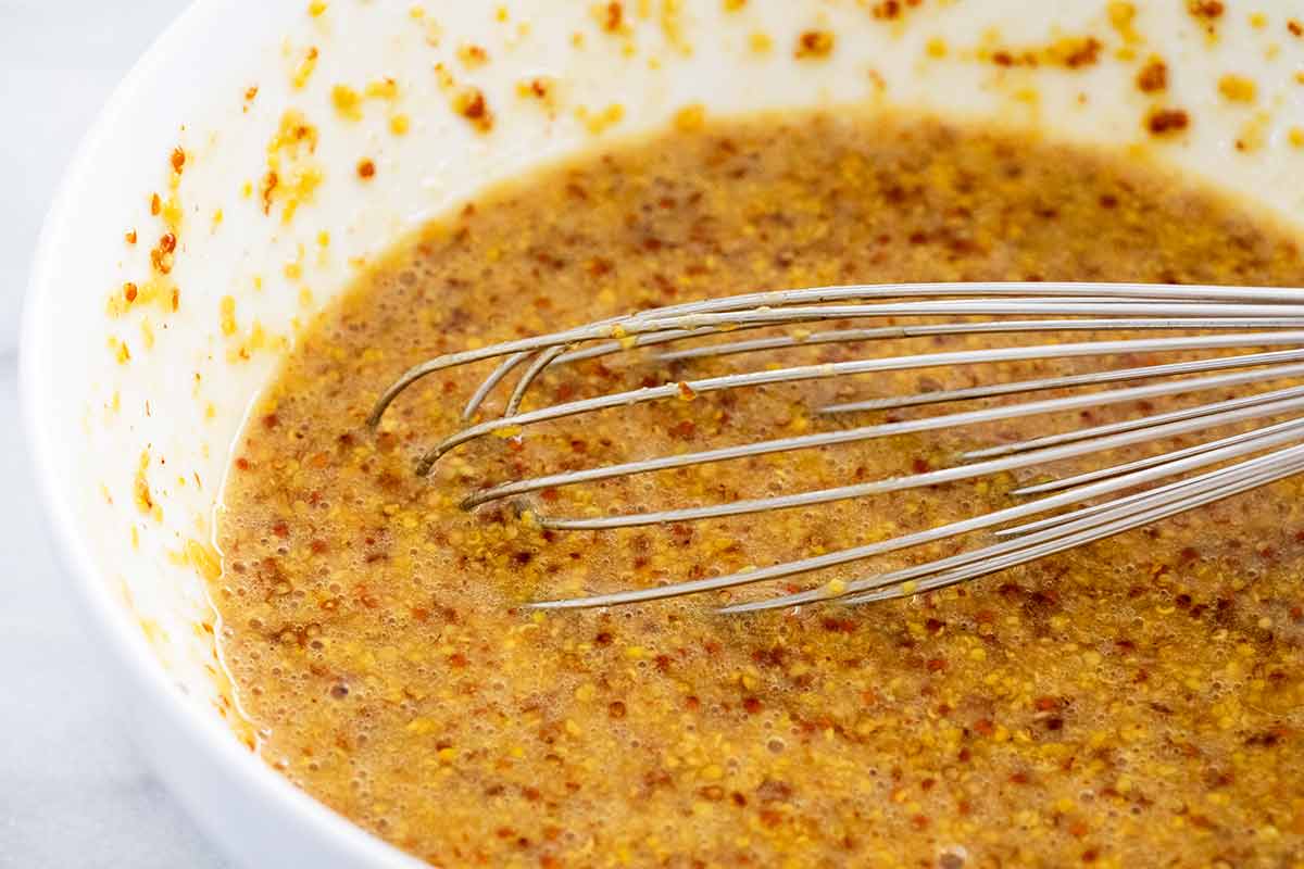 Mustard, beer, and honey being whisked in a white bowl.