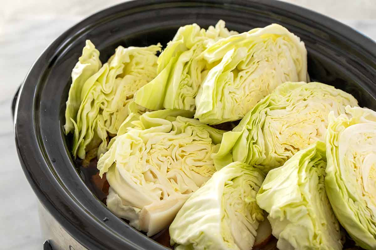 Pieces of cabbage cut into wedges and placed inside a slow cooker.