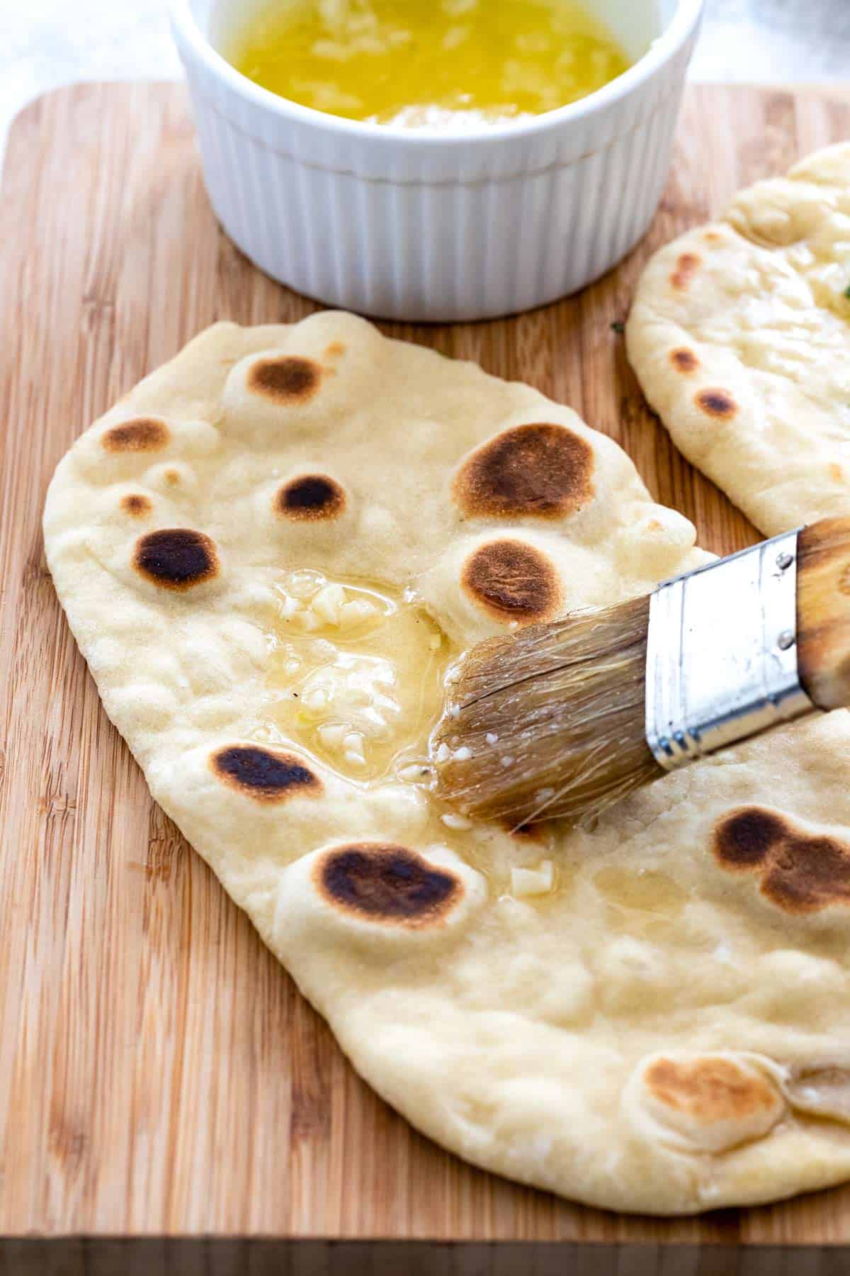 Brushing garlic and butter over a piece of naan bread.
