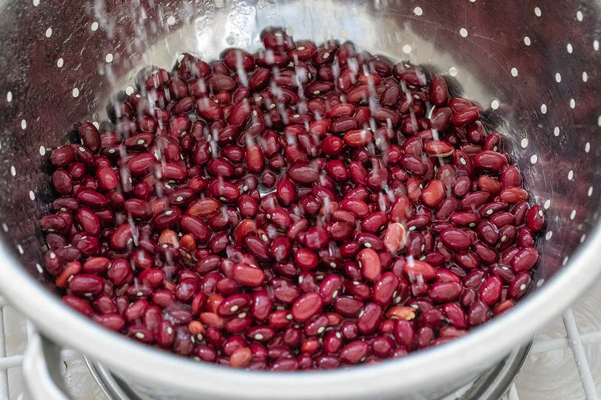 Rinsing dried red beans under running water in a metal colander.