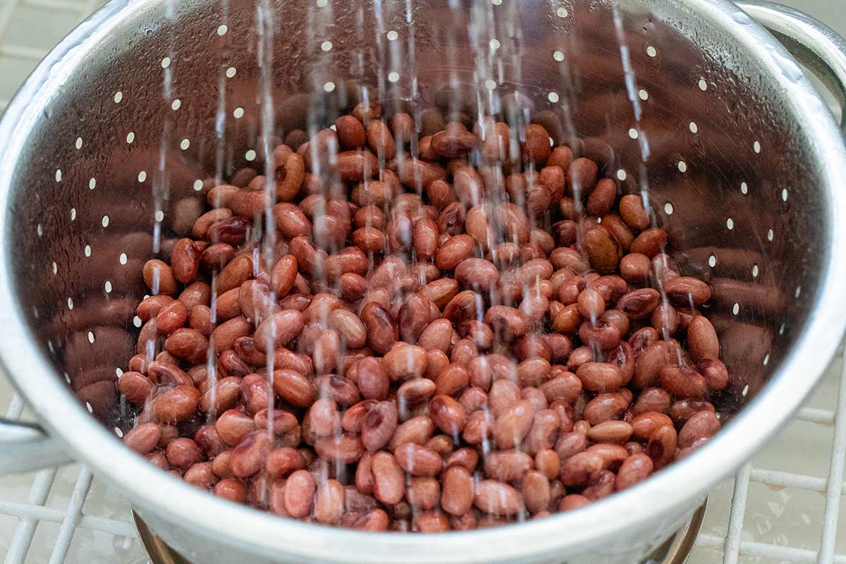 Rinsing soaked beans in a colander under running water.