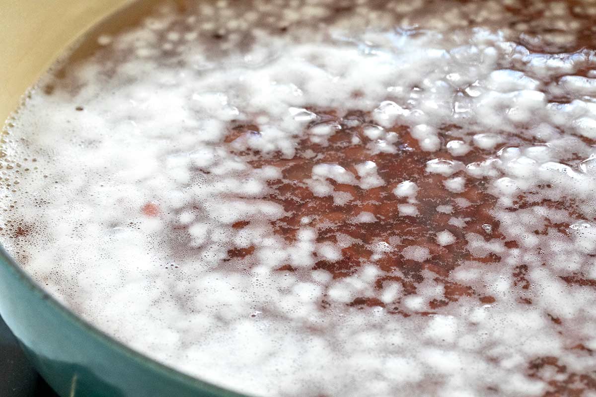 Dried beans in a pot of salted water with a foamy white layer on the surface.