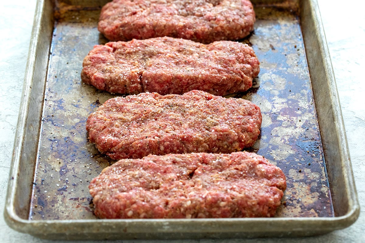 Raw salisbury steak patties on a sheet pan.