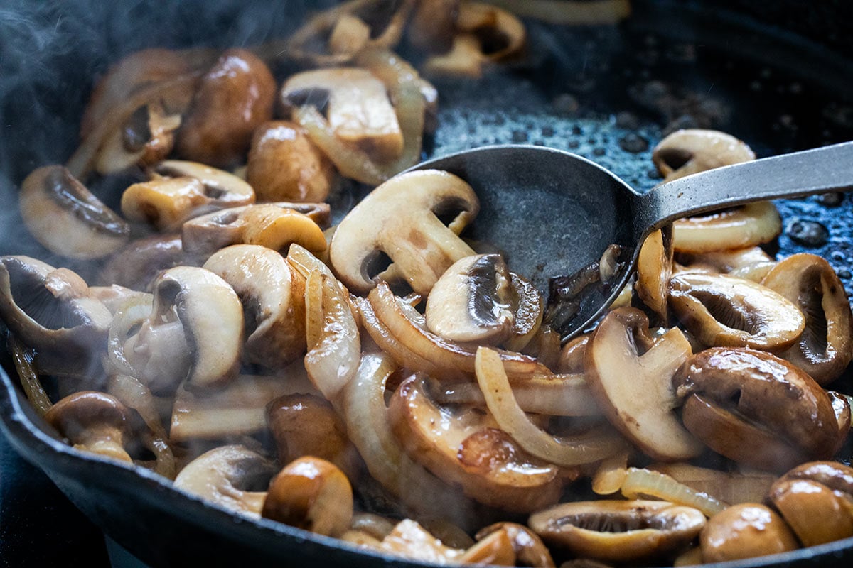 Mushrooms and sliced onions sauteeing in a pan.