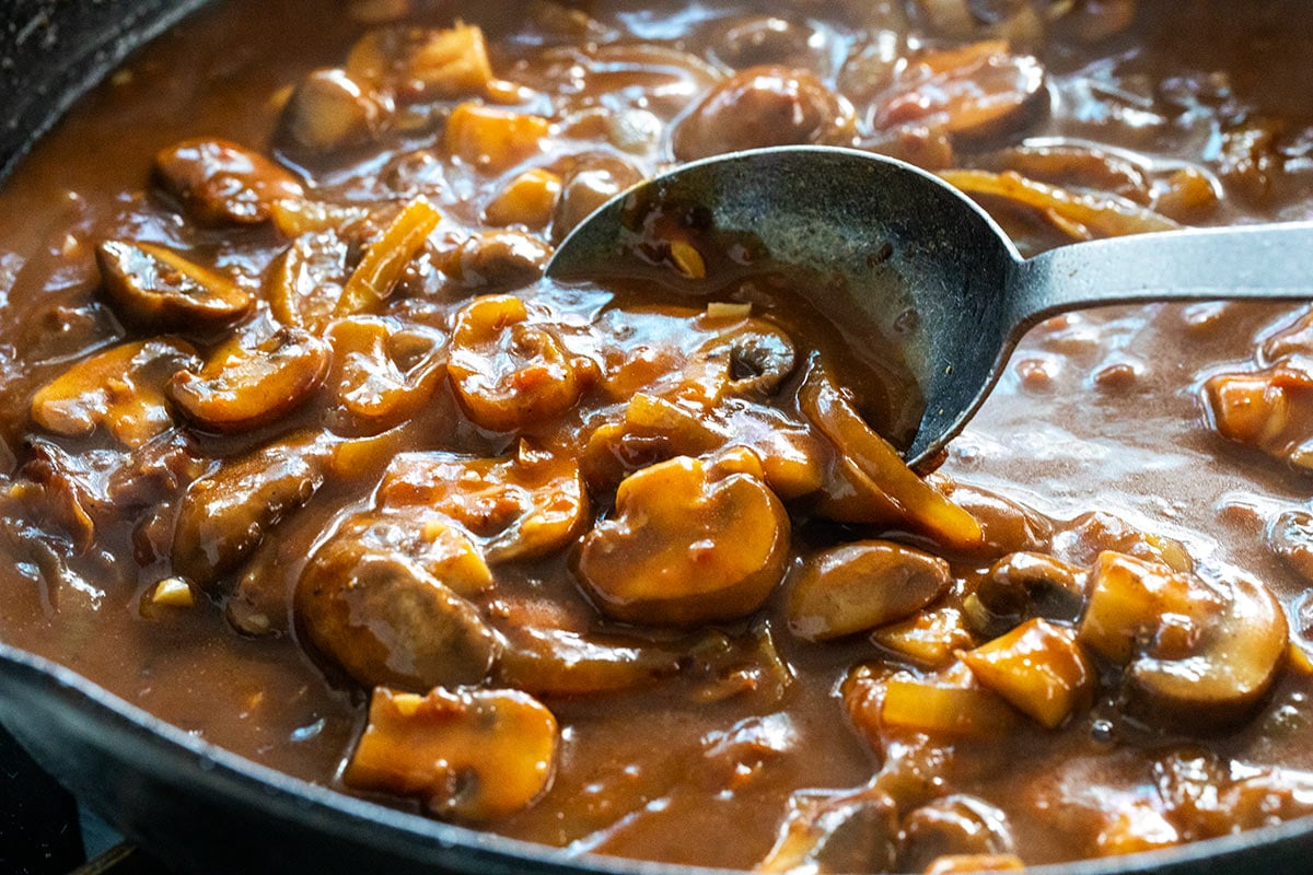 Mushroom pan sauce in a skillet being mixed with a metal spoon.