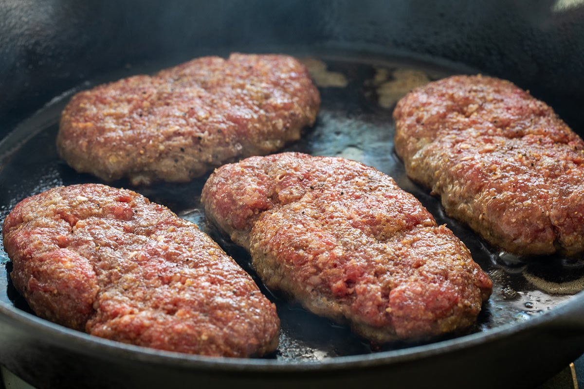 Ground beef patties cooking in a cast iron skillet.