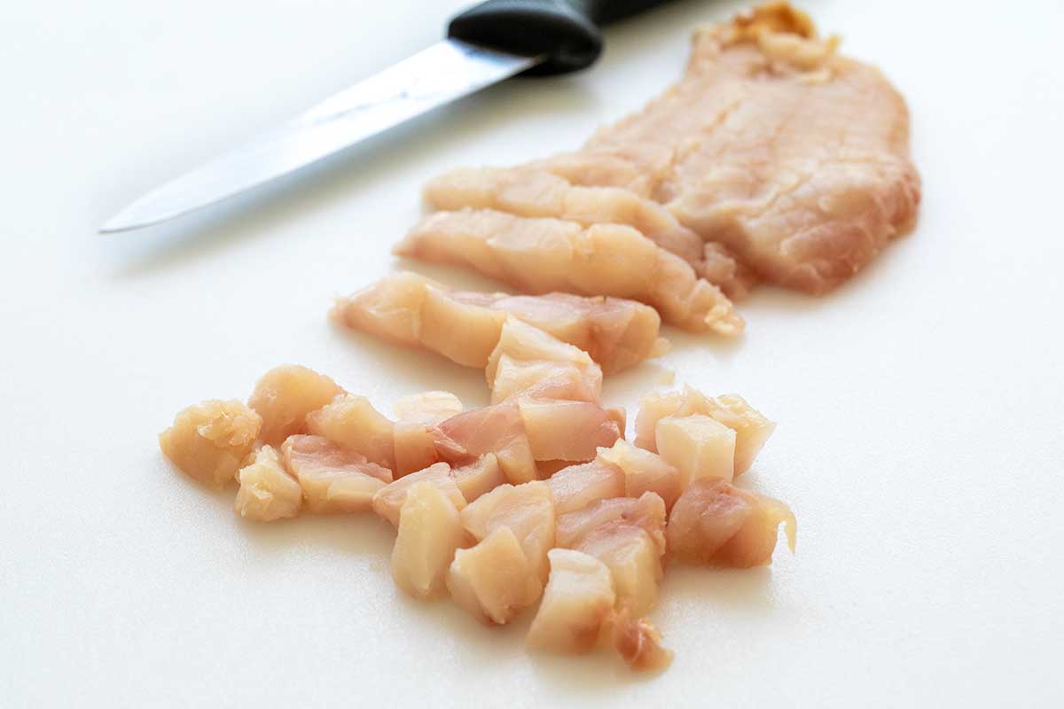 Person slicing a fillet of fish into smaller pieces on a cutting board.