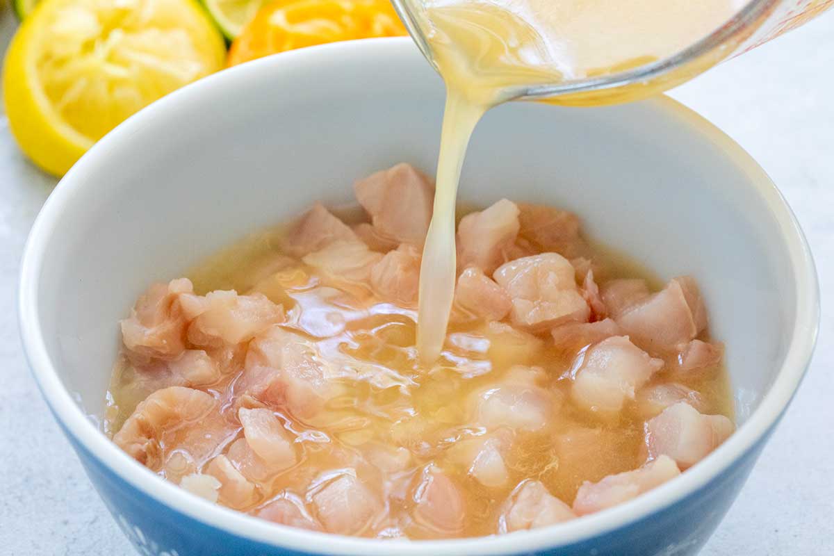 Pouring a measuring cup of acidic liquid into a bowl of raw cubed fish.