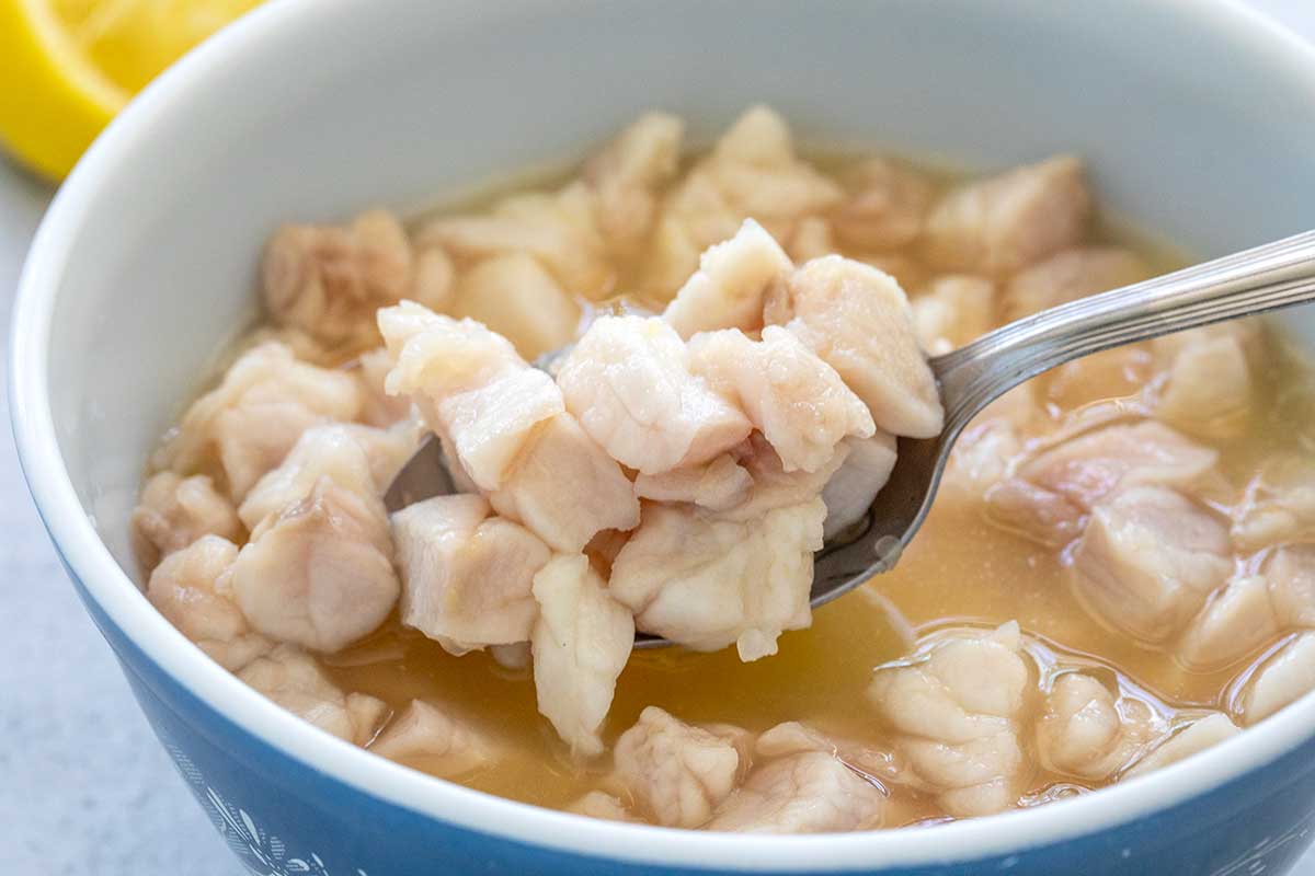 Spoon lifting chunks of fish from a bowl of citrus juices.