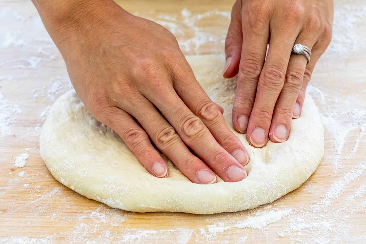 Hands pressing into a ball of dough on a floured surface.