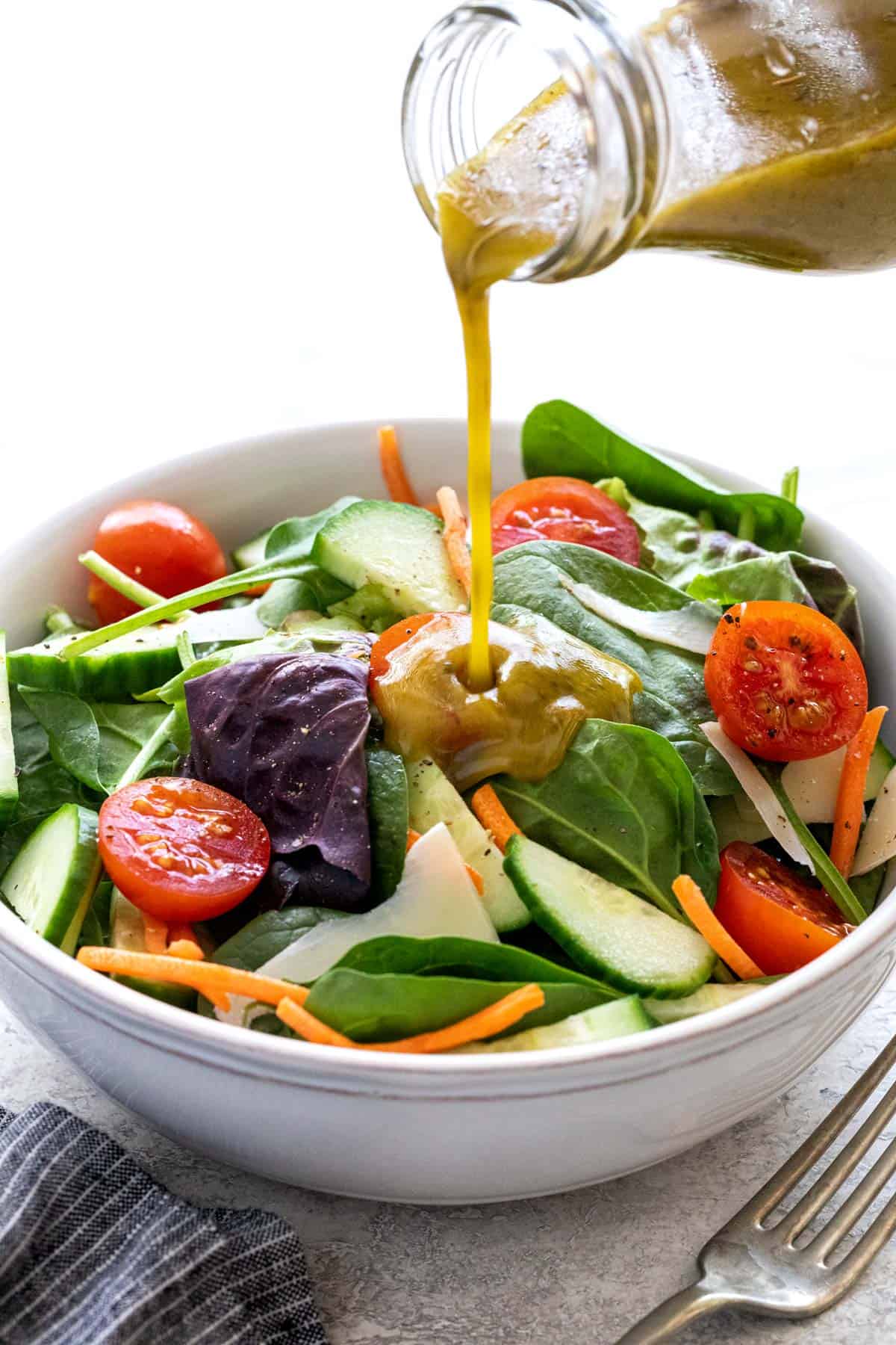Pouring italian dressing over a bowl of salad.