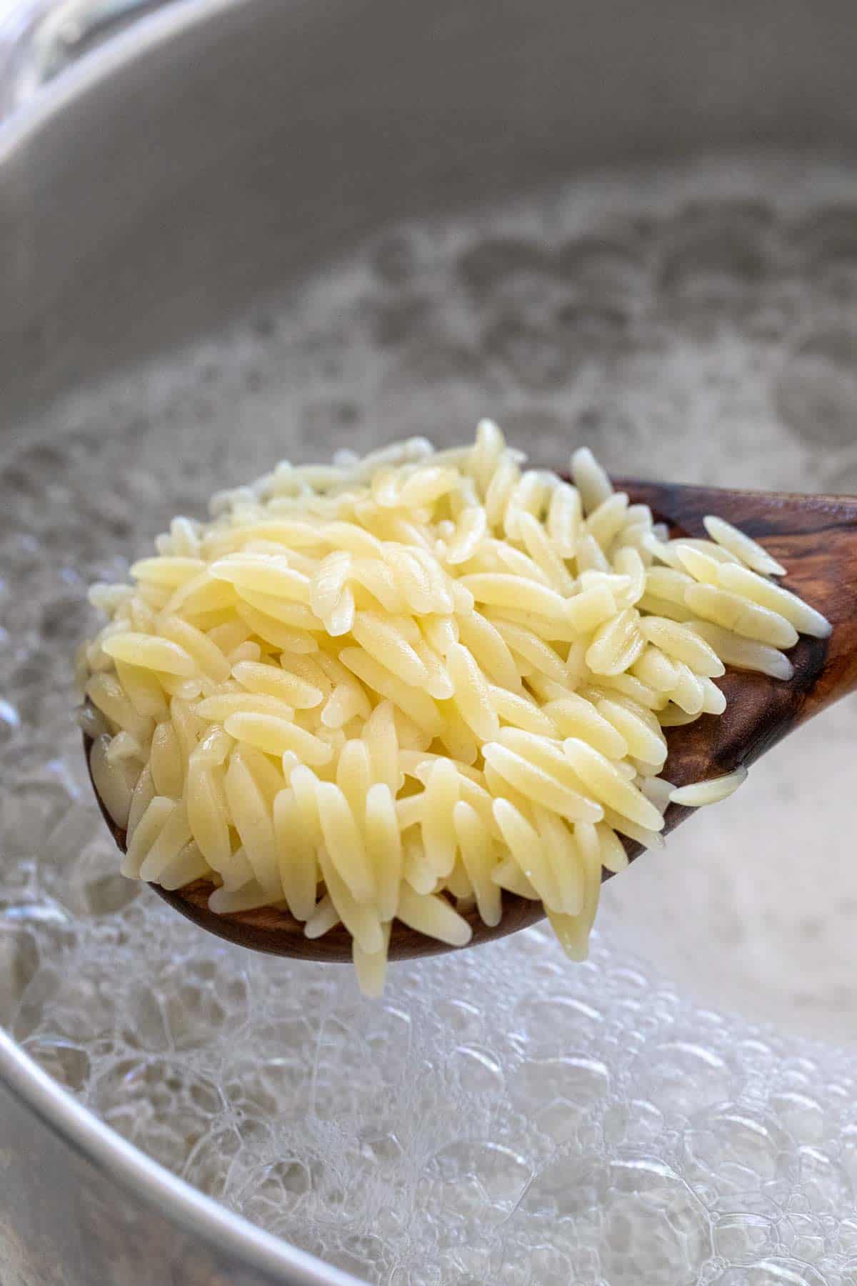 Wooden spoon lifting Orzo pasta cooking in a pot of water.