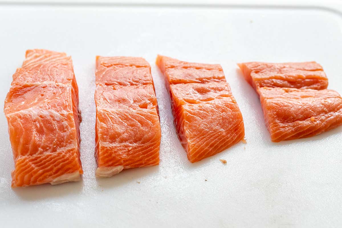 Four raw, skinless salmon fillets cut into even portions on a white cutting board.