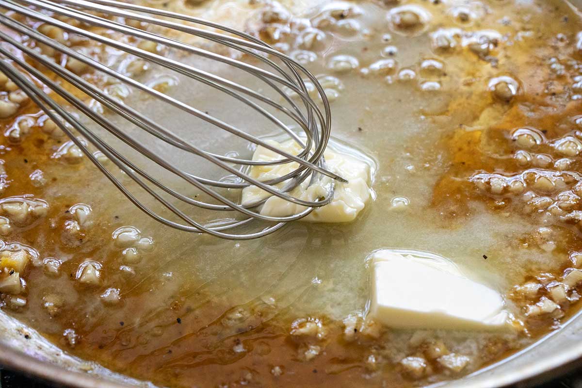 Whisking pats of cold butter into a garlic lemon sauce in a skillet.