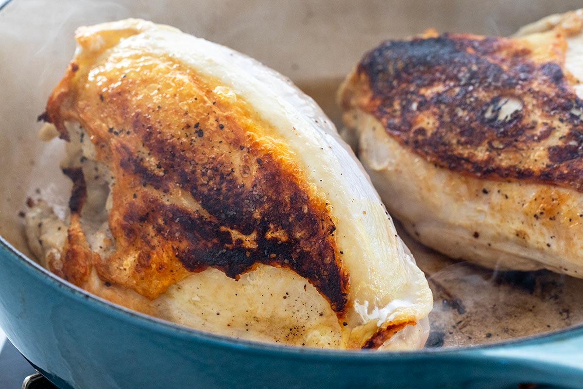 Searing two chicken breasts with skin in a Dutch oven.