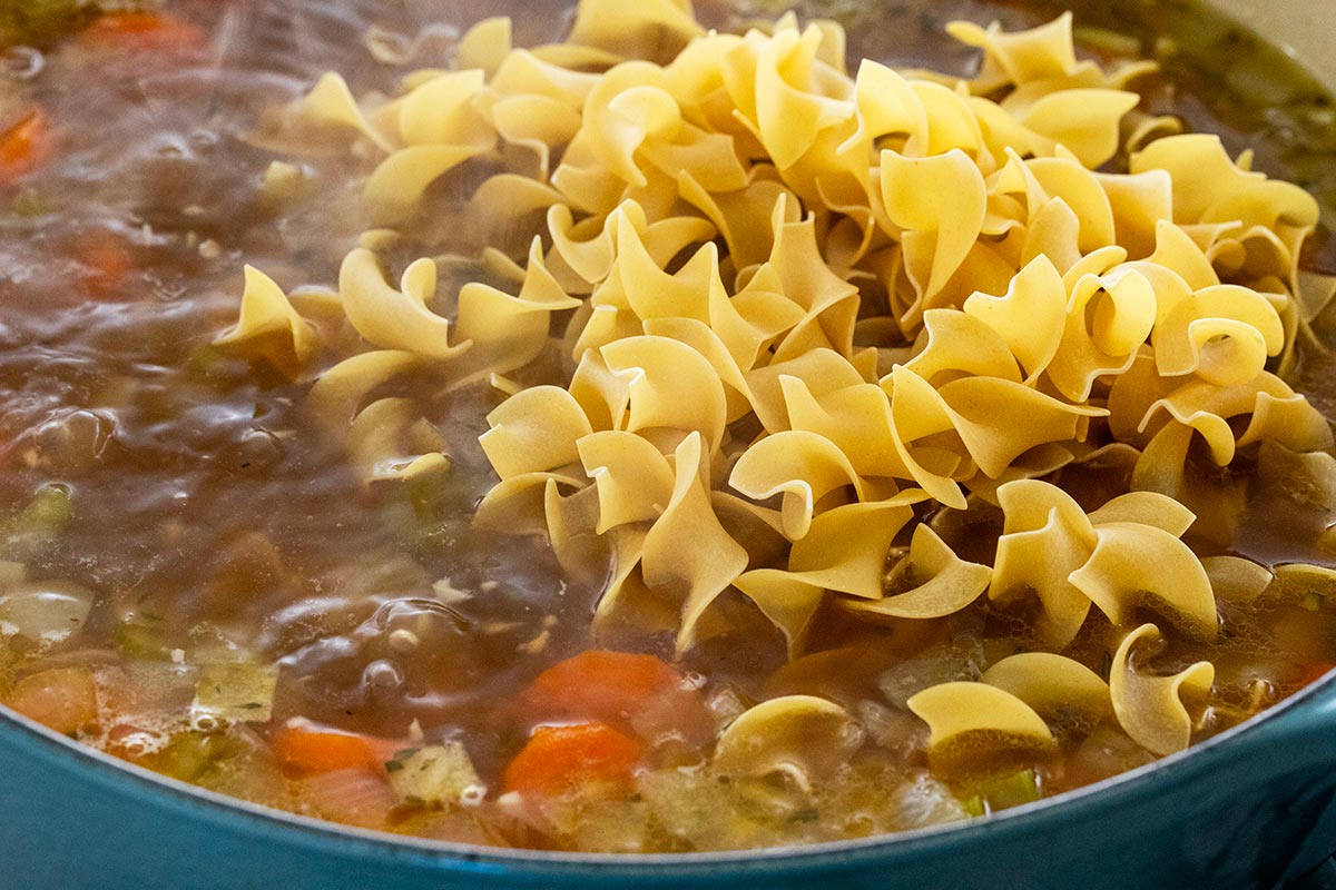 Egg noodles added to a big pot of chicken soup.