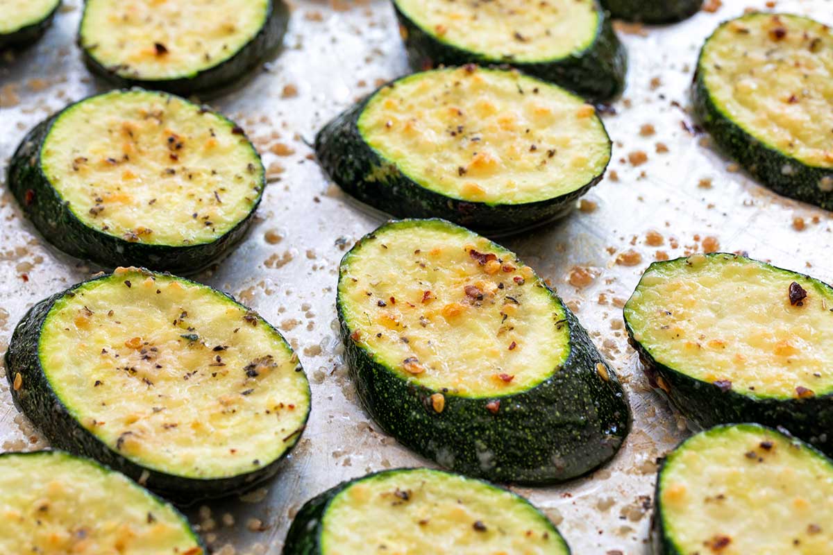 Seasoned zucchini slices topped with cheese and spices arranged on a metal baking sheet.