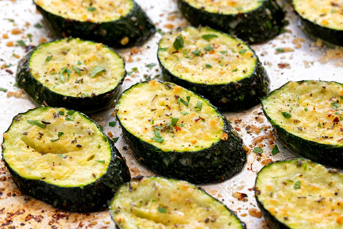 Thickly sliced, seasoned zucchini rounds arranged in a single layer on a baking sheet.