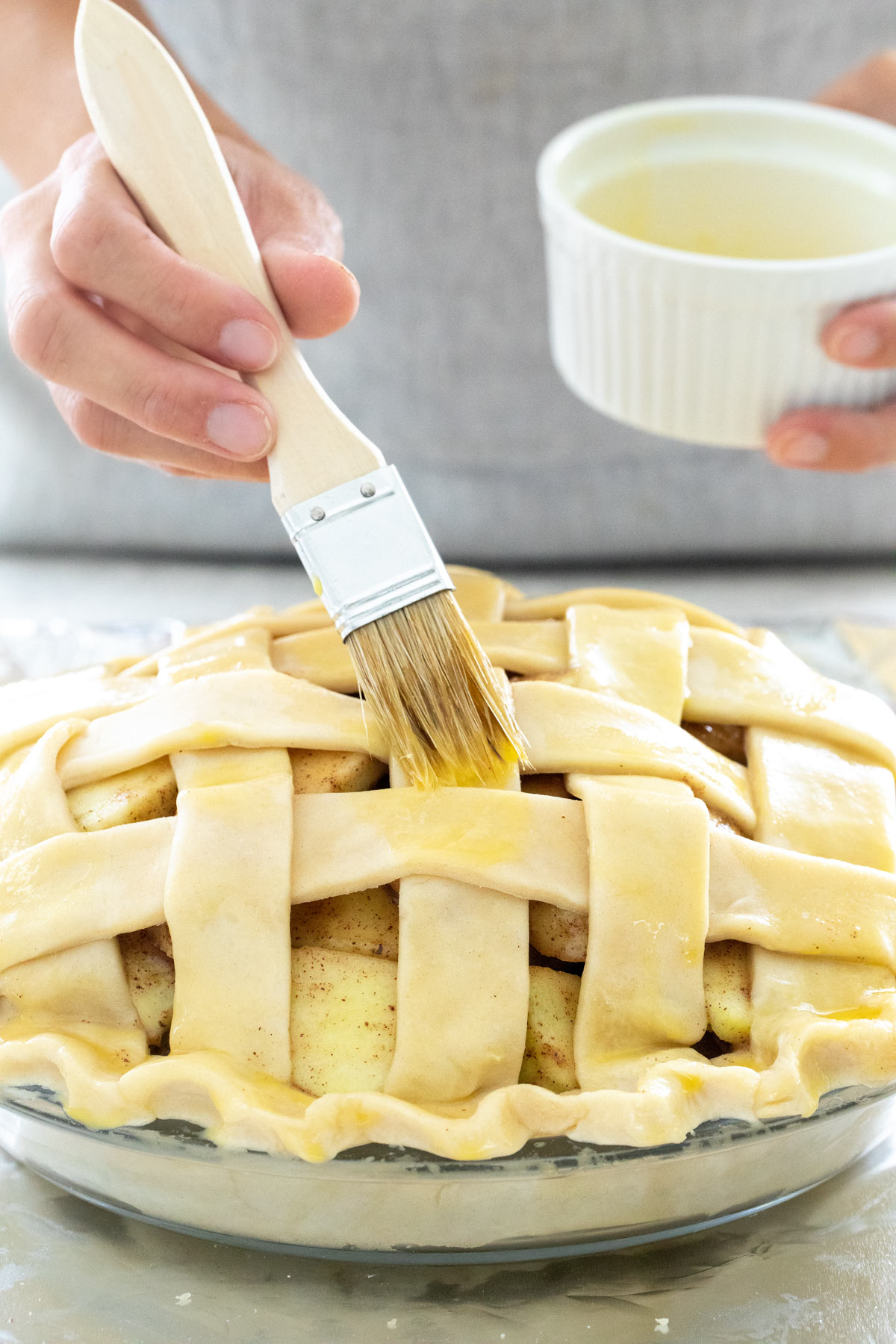 Person brushing a lattice pie top with egg wash before baking.