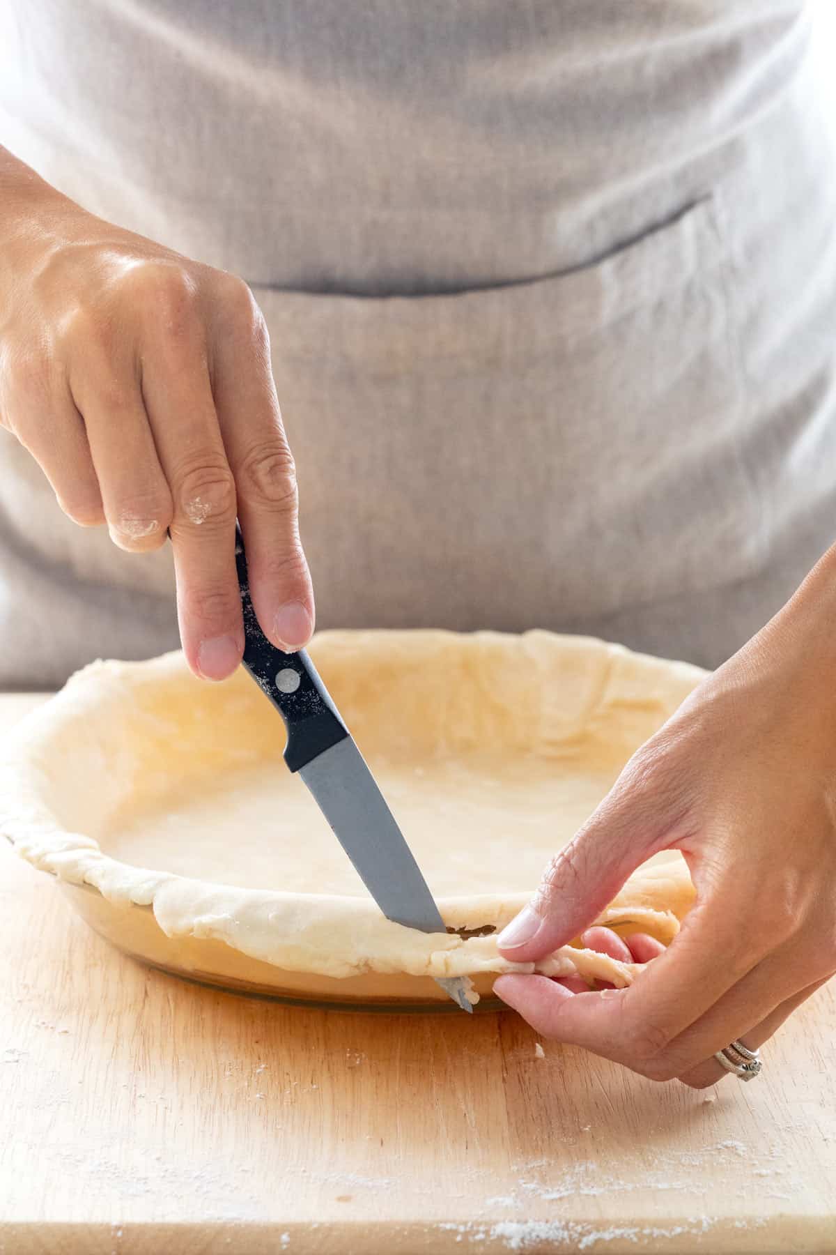 Knife trimming excess pie dough around a dish.