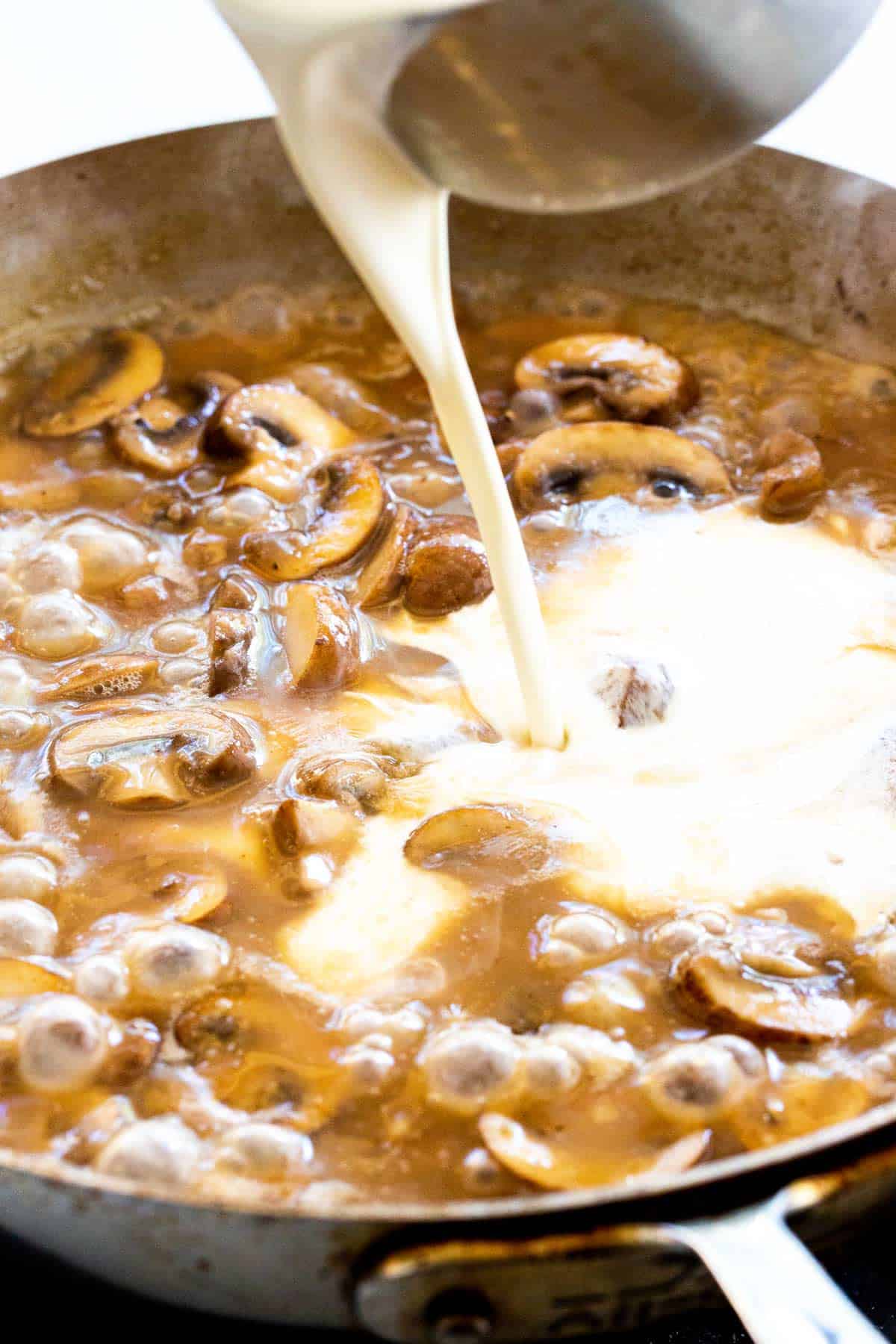 Pouring heavy cream in a pan of mushroom sauce.