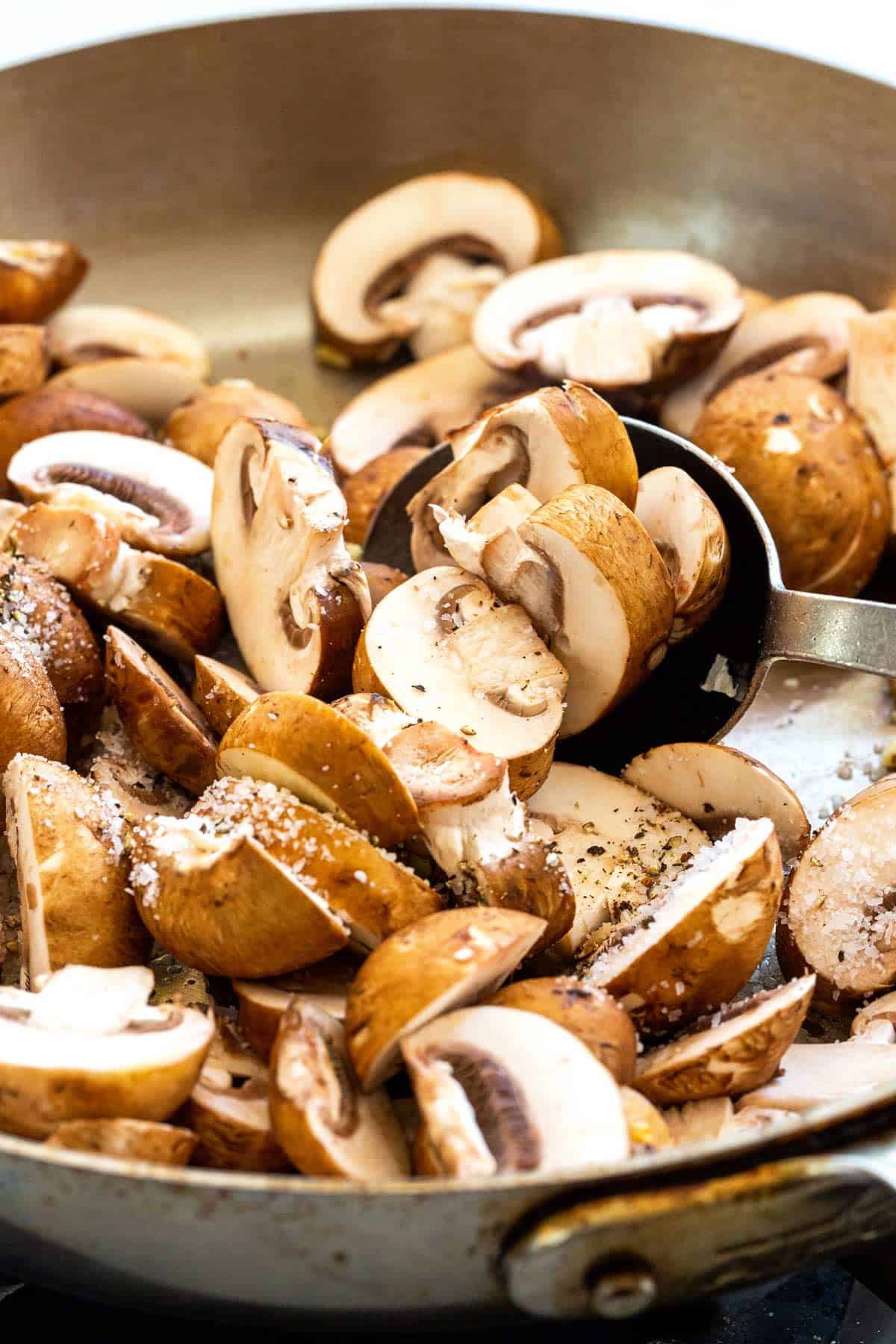 Sliced brown mushrooms cooking in a pan.