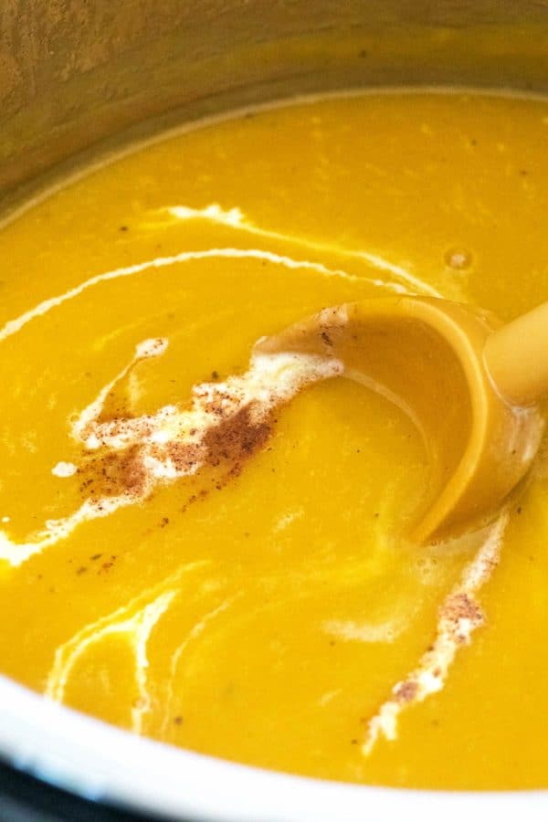 Close up of butternut squash soup in a pot with cream, nutmeg, and cinnamon.