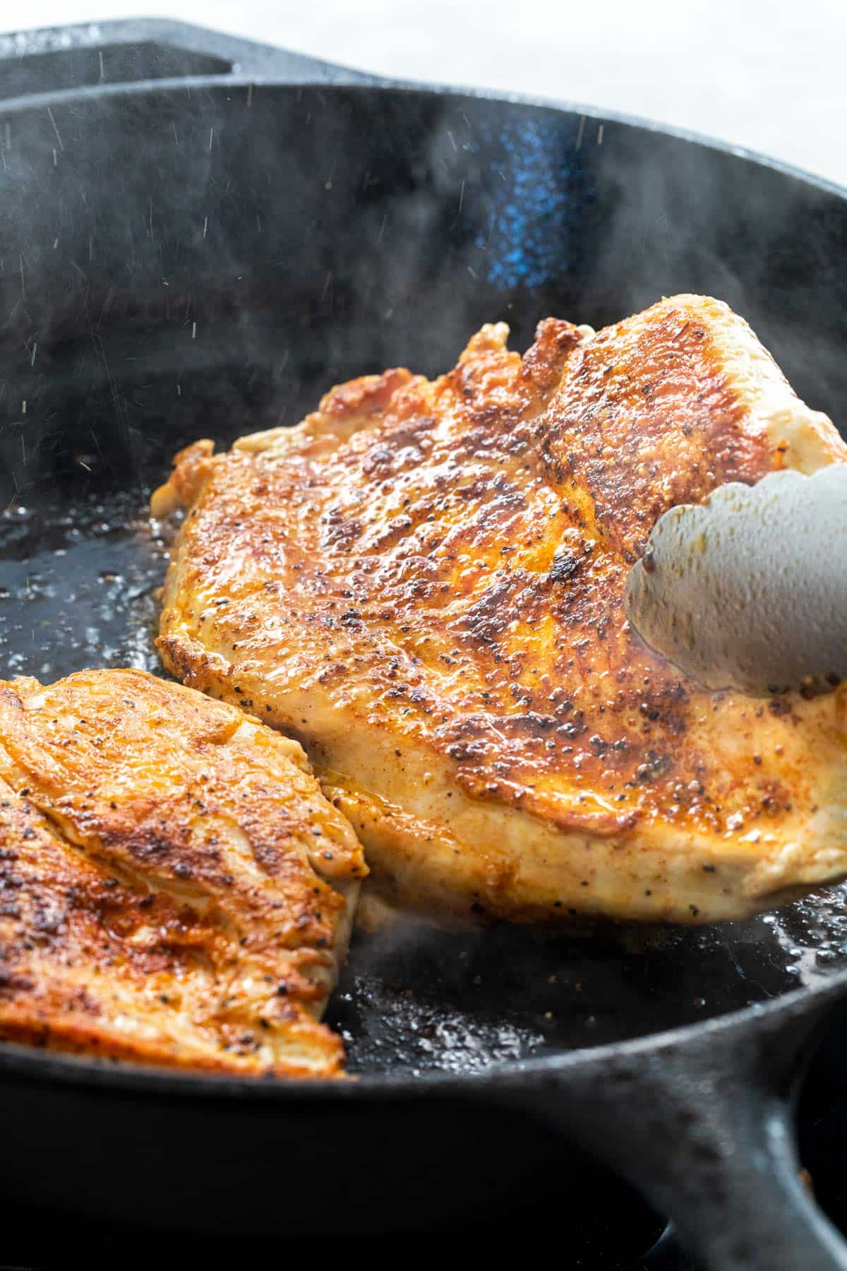 Chicken with seared blacken surface cooking in a cast iron skillet.