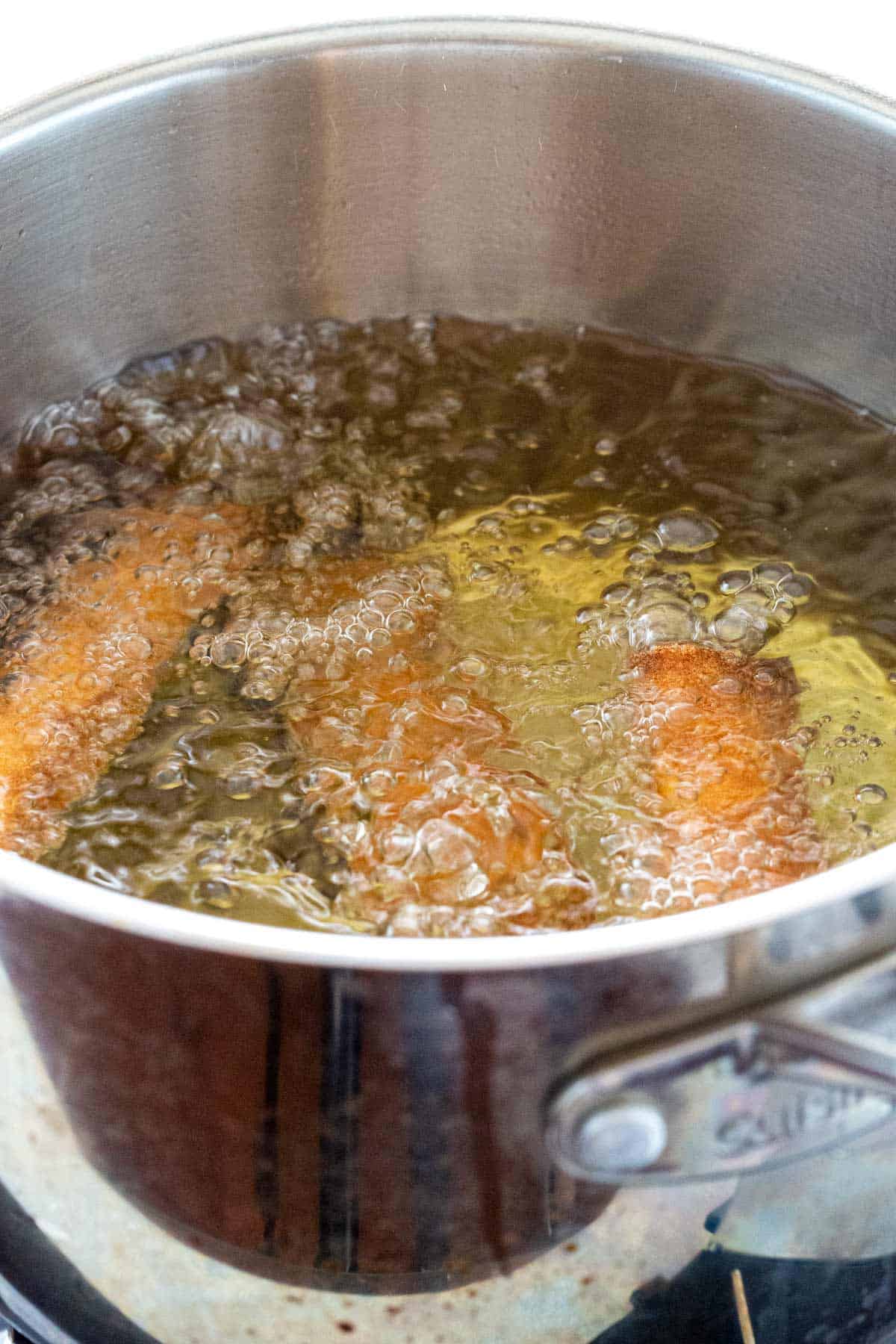 Three egg rolls frying in a pot of hot oil.