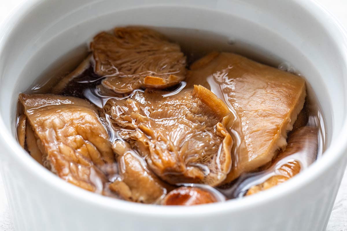 Dried mushrooms rehydrating in a white ramekin filled with hot water.
