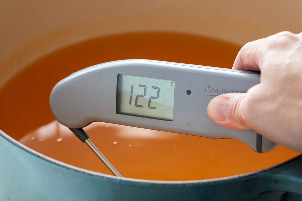 Digital thermometer reading 122 degrees Fahrenheit inserted into a pot of warm stock.