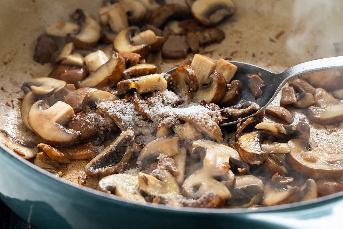 Sliced mushrooms sautéing in a pan with coarse salt sprinkled on top.