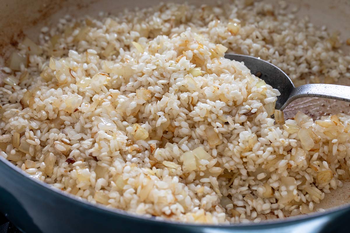 Arborio rice mixed with sautéed diced onions being stirred in a pan with a spoon.