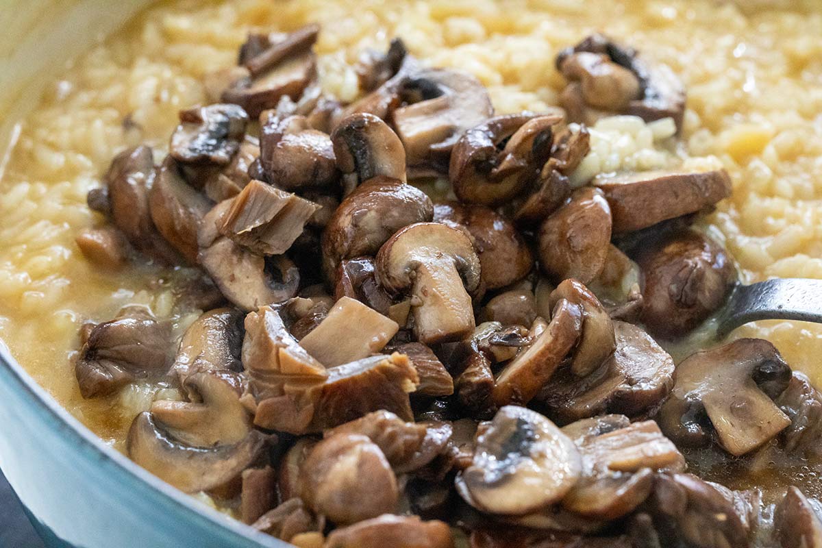 Sautéed sliced mushrooms added to creamy risotto in a pot.