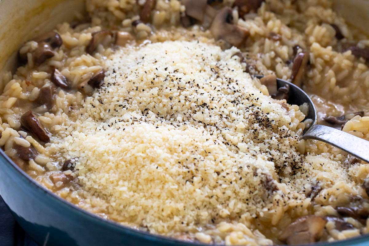 Grated parmesan cheese and ground black pepper added on top of cooked mushroom risotto in a pot.