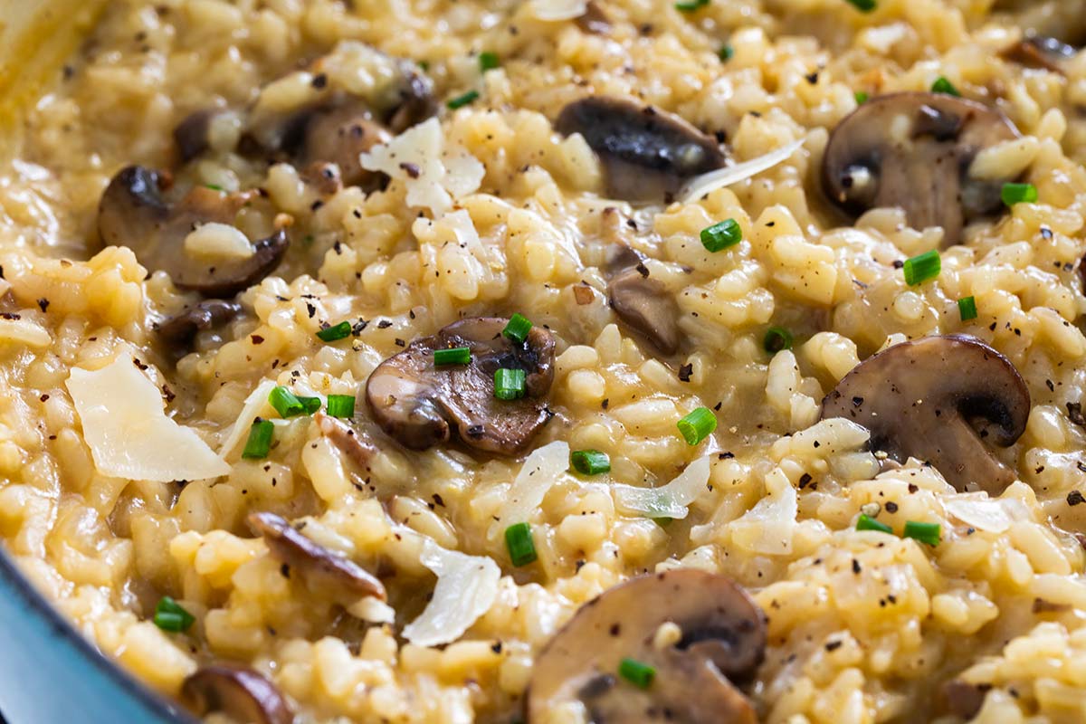 Creamy mushroom risotto topped with sliced mushrooms, shaved Parmesan, black pepper, and chopped chives.