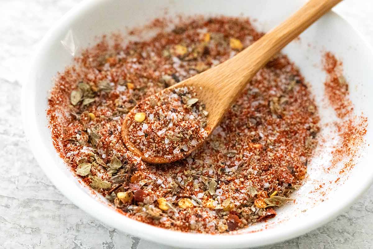 Small white bowl with wooden spoon and homemade cajun seasoning ingredients.